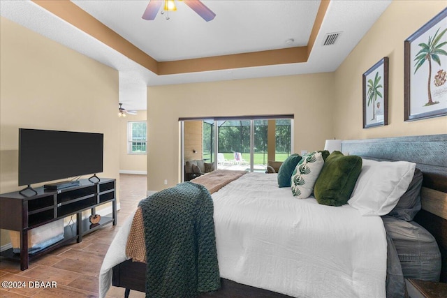 bedroom featuring ceiling fan, wood-type flooring, access to outside, and a tray ceiling