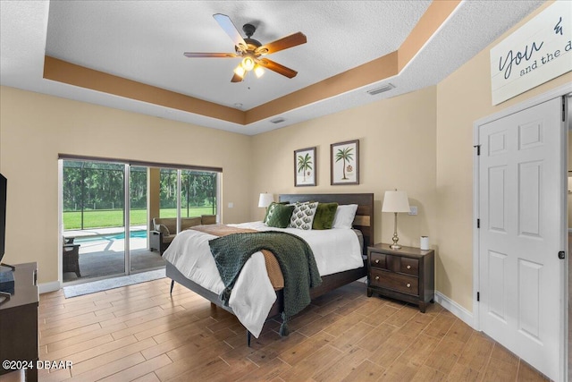 bedroom featuring access to outside, ceiling fan, light hardwood / wood-style flooring, and a tray ceiling