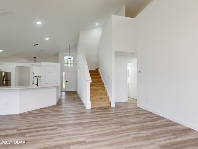 5336 Georgia Peach Ave, Port Orange, FL 32128 - unfurnished living room featuring a sink, high vaulted ceiling, light wood-style floors, stairway, and baseboards