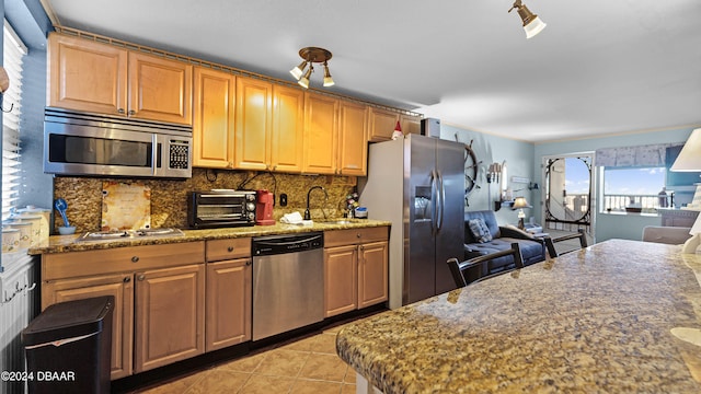 kitchen with light tile patterned flooring, appliances with stainless steel finishes, stone countertops, and sink