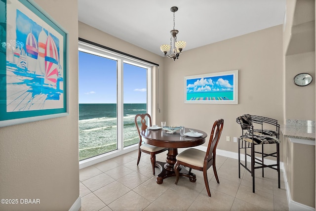 dining area featuring a beach view, light tile patterned floors, a chandelier, and a water view