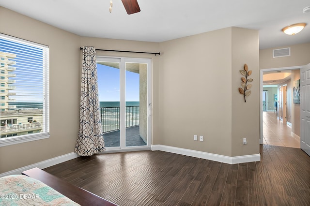 unfurnished bedroom featuring ceiling fan, a water view, multiple windows, and access to exterior