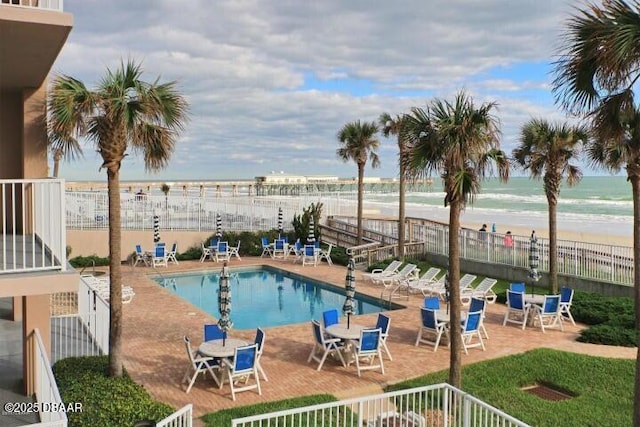 view of pool with a patio, a water view, and a view of the beach