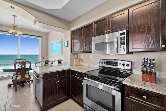 kitchen with light stone counters, kitchen peninsula, stainless steel appliances, a notable chandelier, and a water view