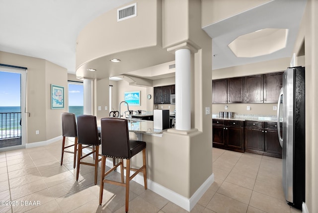 kitchen featuring stainless steel appliances, a water view, ornate columns, light tile patterned floors, and a breakfast bar area