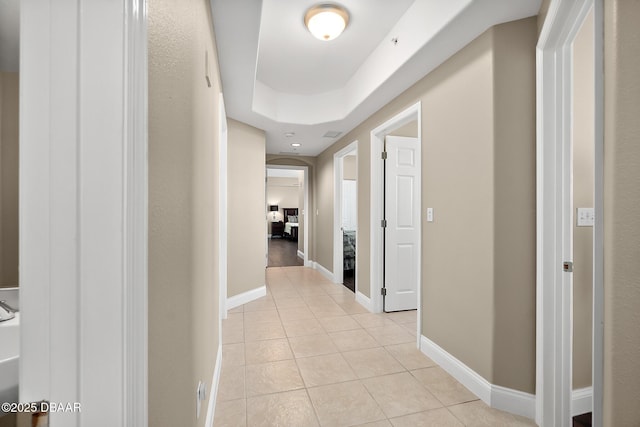 hall with light tile patterned flooring and a tray ceiling