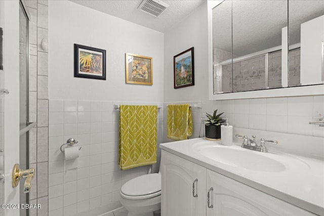 bathroom with toilet, a shower with door, tile walls, a textured ceiling, and vanity