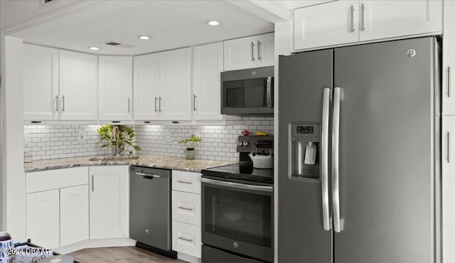 kitchen with stainless steel appliances, white cabinetry, and light stone counters