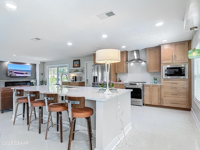 kitchen with stainless steel appliances, wall chimney range hood, a sink, a breakfast bar area, and light countertops