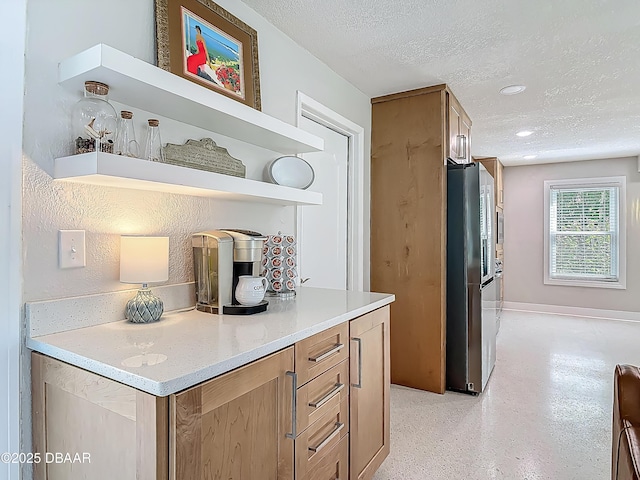 kitchen featuring open shelves, a textured ceiling, freestanding refrigerator, baseboards, and brown cabinetry