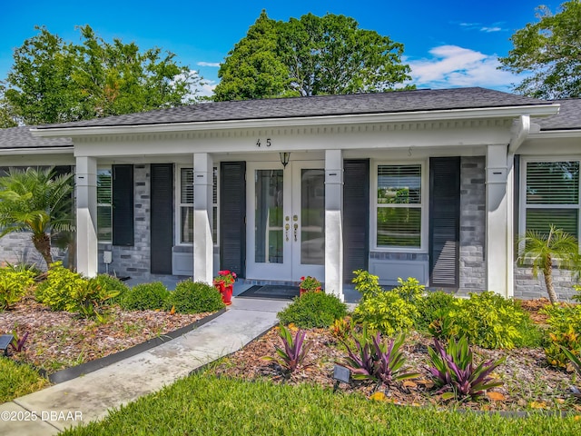 bungalow-style house featuring french doors, a porch, a shingled roof, and brick siding