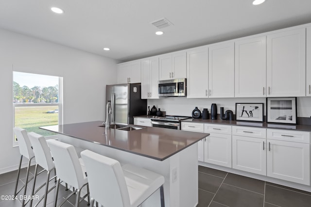 kitchen with white cabinets, dark tile patterned floors, an island with sink, appliances with stainless steel finishes, and a breakfast bar area