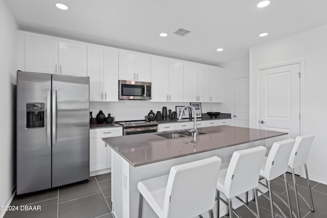 kitchen with a kitchen island with sink, white cabinets, sink, dark tile patterned floors, and appliances with stainless steel finishes