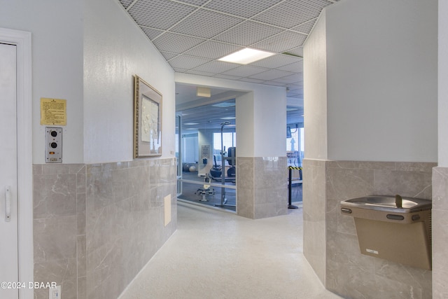 corridor featuring a paneled ceiling and tile walls