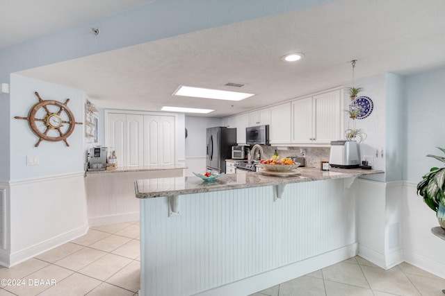 kitchen with stainless steel appliances, white cabinetry, kitchen peninsula, light stone countertops, and a breakfast bar area