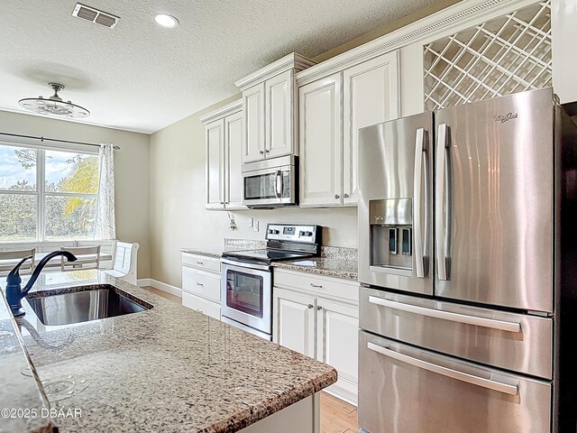 417 Grande Sunningdale Loop, Daytona Beach, FL 32124 - kitchen with appliances with stainless steel finishes, a sink, a textured ceiling, light stone countertops, and white cabinets