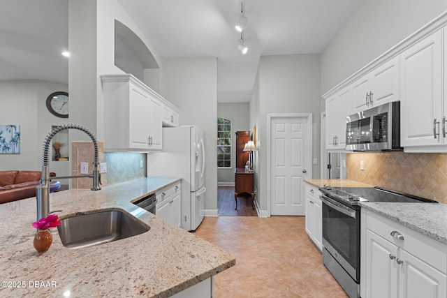 kitchen with appliances with stainless steel finishes, white cabinetry, a sink, and light stone countertops