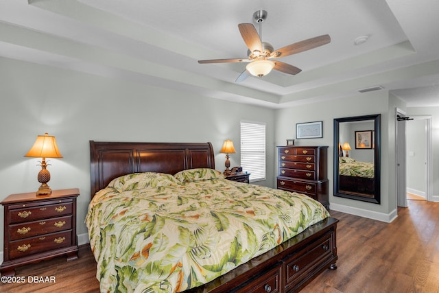 bedroom featuring a tray ceiling, dark wood-style flooring, visible vents, and baseboards