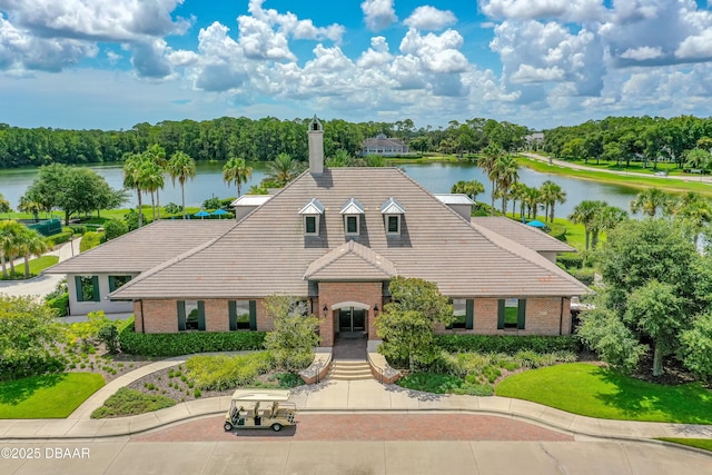 view of front facade featuring a chimney, a water view, brick siding, and a tiled roof