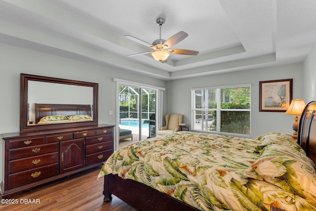 bedroom with access to exterior, multiple windows, a tray ceiling, and wood finished floors