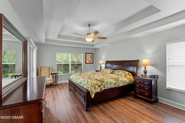 bedroom featuring dark wood-style floors, ceiling fan, baseboards, and a raised ceiling