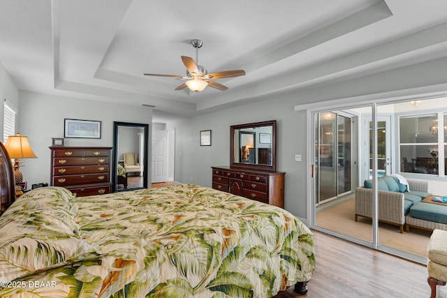 bedroom with ceiling fan, visible vents, access to outside, light wood finished floors, and a raised ceiling