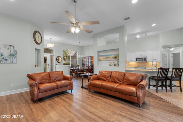 living room featuring ceiling fan with notable chandelier, light wood-style flooring, visible vents, and baseboards