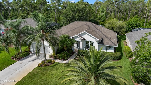 view of front of property featuring concrete driveway, roof with shingles, an attached garage, a front lawn, and stucco siding