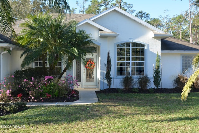 view of front of house featuring a shingled roof, a front yard, and stucco siding