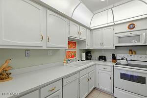 4175 S Atlantic Ave Unit 405, New Smyrna Beach, FL 32169 - kitchen with white appliances, light countertops, light tile patterned flooring, a sink, and white cabinets