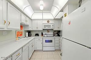 4175 S Atlantic Ave Unit 405, New Smyrna Beach, FL 32169 - kitchen featuring white appliances, light tile patterned flooring, light countertops, and white cabinetry