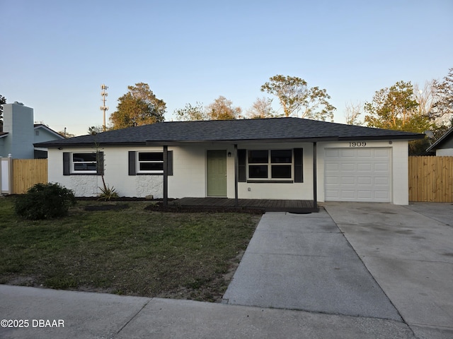 ranch-style home featuring a shingled roof, fence, a front yard, a garage, and driveway