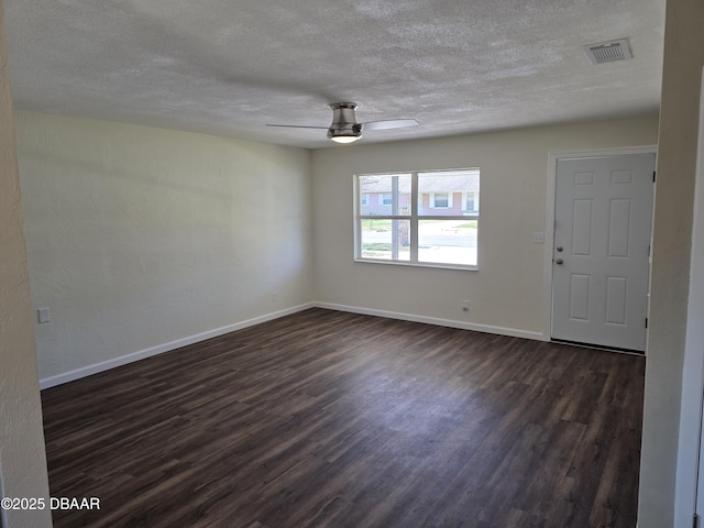 unfurnished room with dark wood-style floors, visible vents, a ceiling fan, and baseboards