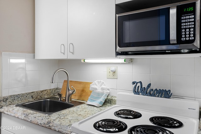 kitchen with stove, sink, decorative backsplash, light stone counters, and white cabinetry