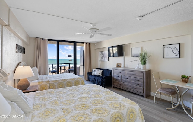 bedroom with hardwood / wood-style flooring, ceiling fan, access to exterior, a textured ceiling, and a wall of windows