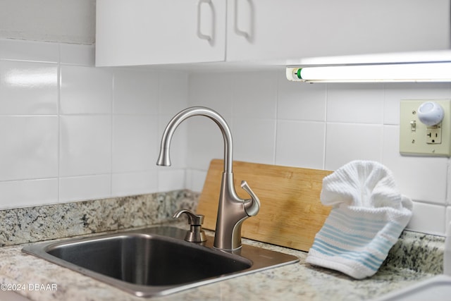 details with decorative backsplash, light stone counters, white cabinetry, and sink