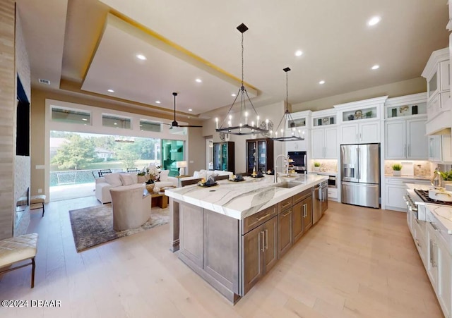 kitchen featuring white cabinetry, a large island with sink, decorative light fixtures, appliances with stainless steel finishes, and light wood-type flooring