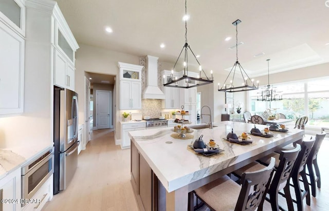 kitchen featuring white cabinetry, a large island, stainless steel appliances, pendant lighting, and custom range hood