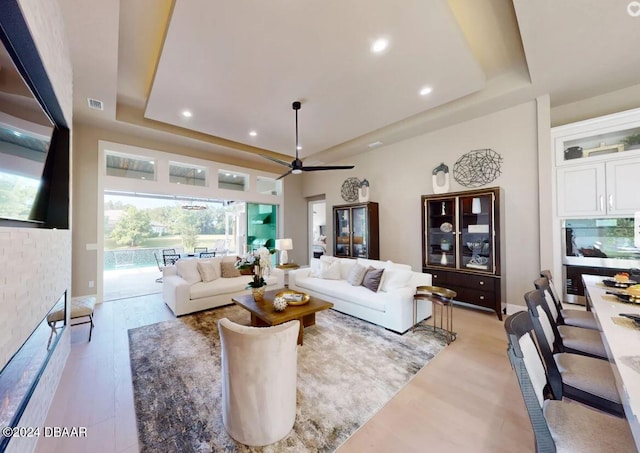 living room featuring ceiling fan, a raised ceiling, and light wood-type flooring