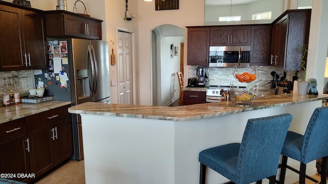 kitchen with kitchen peninsula, appliances with stainless steel finishes, tasteful backsplash, and light stone countertops