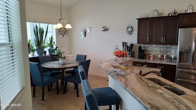 kitchen with hanging light fixtures, sink, stainless steel fridge with ice dispenser, and light stone countertops