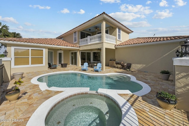 back of property with ceiling fan, a swimming pool with hot tub, a balcony, and a patio area