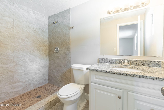 bathroom with a textured ceiling, vanity, toilet, and tiled shower