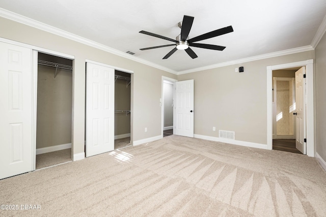 unfurnished bedroom with carpet, ceiling fan, ornamental molding, and two closets