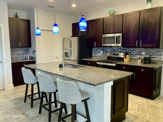 kitchen featuring light stone counters, stainless steel appliances, a sink, and a kitchen breakfast bar