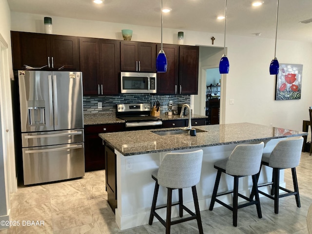 kitchen with stainless steel appliances, tasteful backsplash, a sink, dark stone countertops, and a kitchen breakfast bar