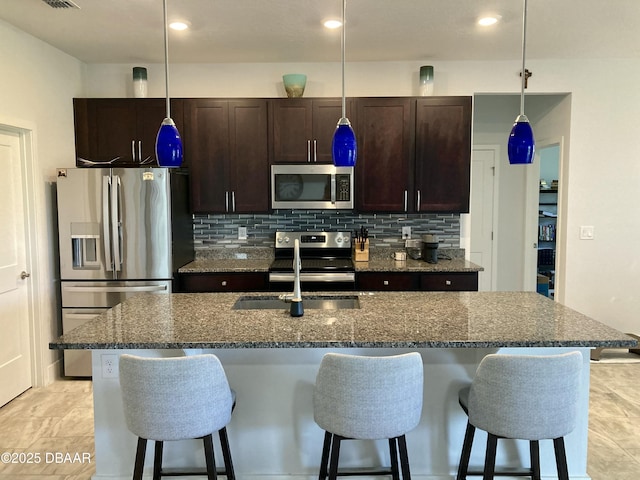 kitchen featuring appliances with stainless steel finishes, an island with sink, decorative backsplash, and a kitchen bar