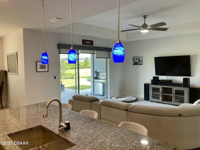 living area featuring a raised ceiling, visible vents, and ceiling fan