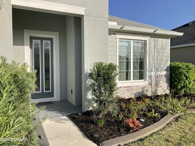 entrance to property featuring a shingled roof and stucco siding