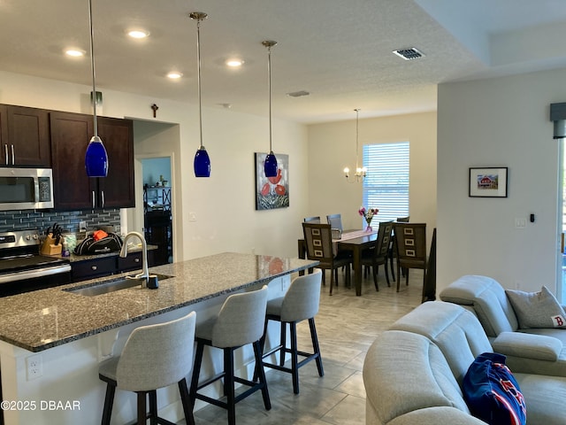 kitchen with visible vents, appliances with stainless steel finishes, open floor plan, a sink, and backsplash